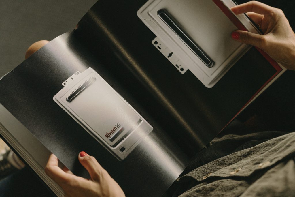 Hands holdng Rheem brand book, flipped to the product page.