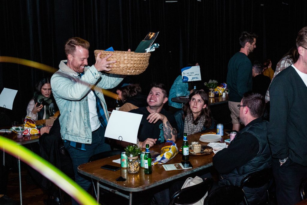 Round winners smiling and holding up their prize basket at the table 