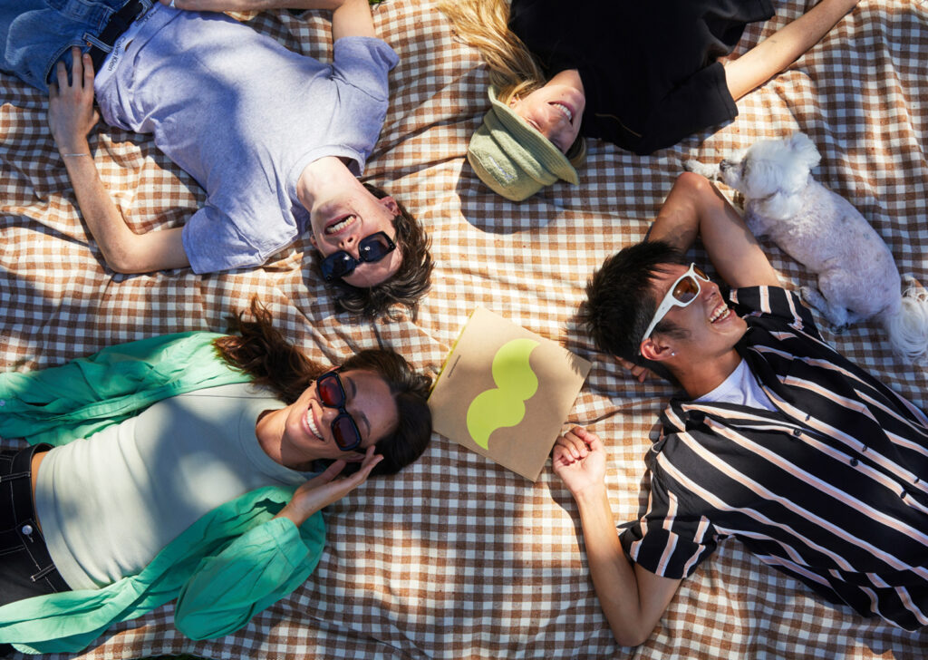 Image of friends laying on a picnic blanket with the Moustache cookie box