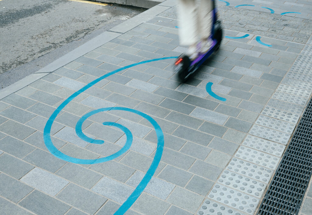 Image of the blue swirl patter on the Waihorotiu Path with a blurred scooter going across the path.